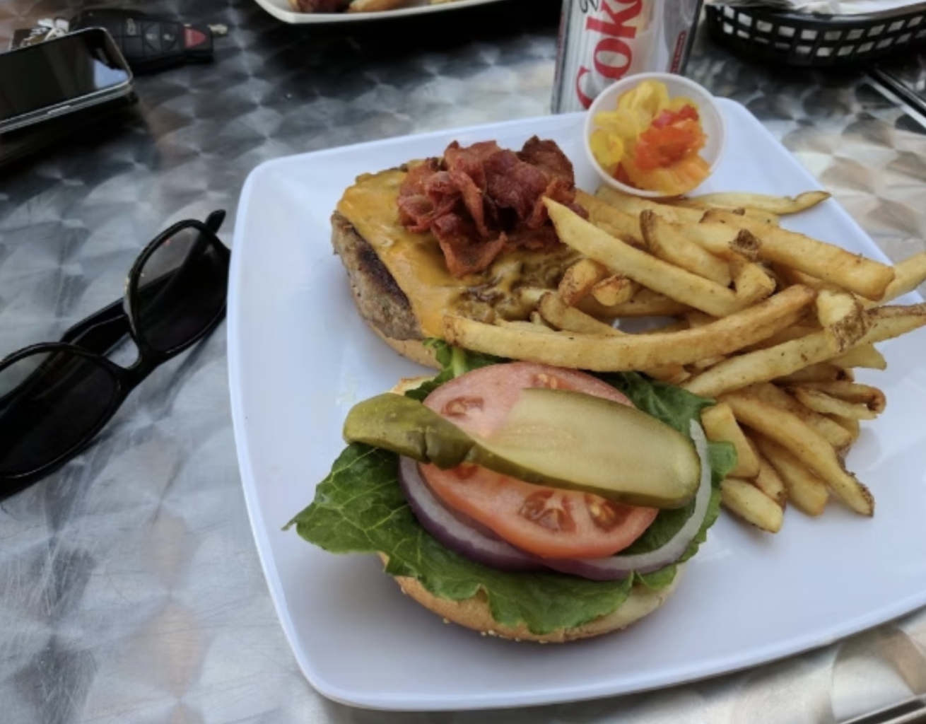 A classic burger served with fresh lettuce, tomato, onion, pickles, bacon, fries and a side of coleslaw.