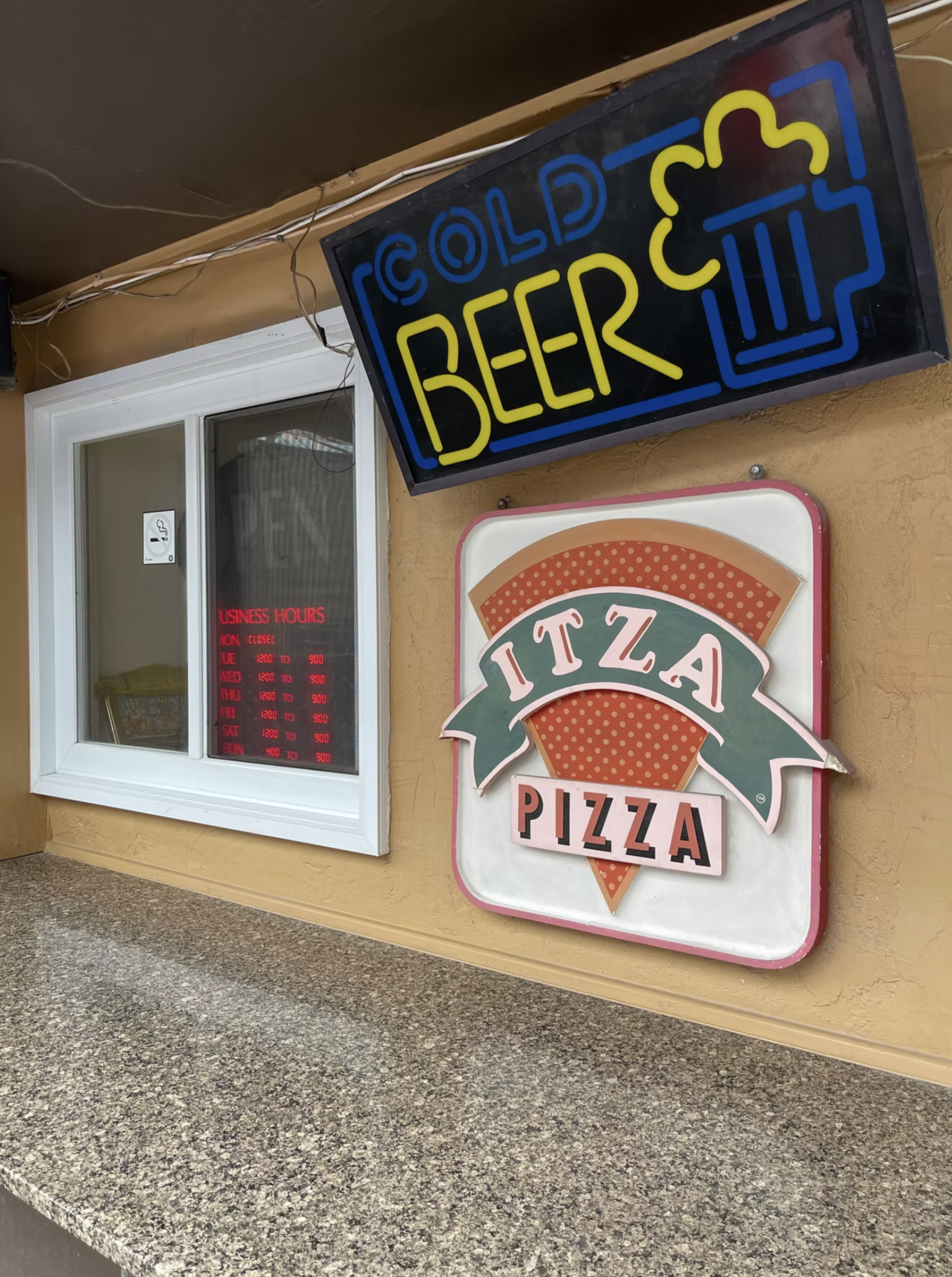 A look at Econo Pizza’s entrance, featuring the classic pizza sign and cold beer available for guests.